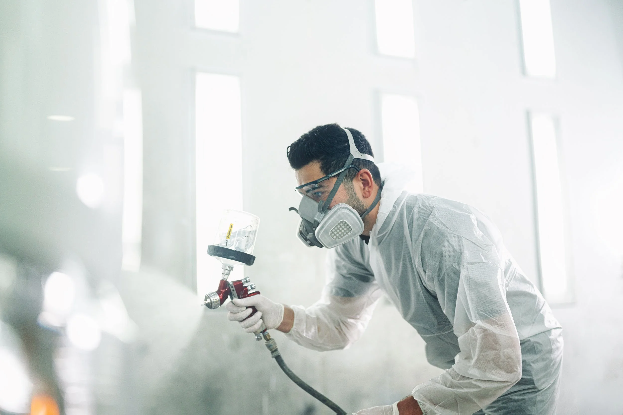 Industrial technician wearing protective gear and operating a spray gun inside a bright workshop in Dubai.