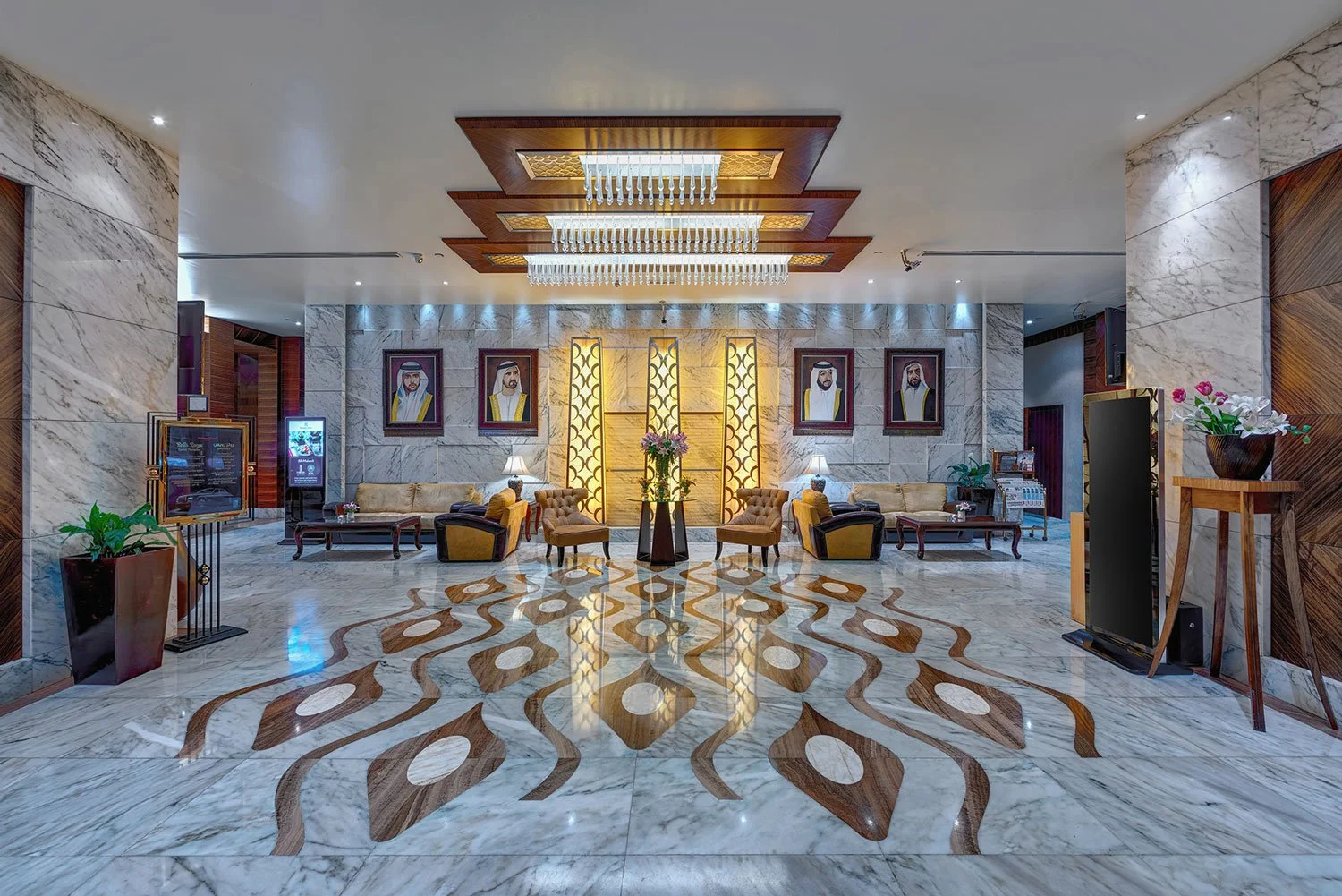 Elegant hotel lobby with marble floors, seating area with sofas and chairs, framed photos on the wall, decorative lighting, and potted plants.