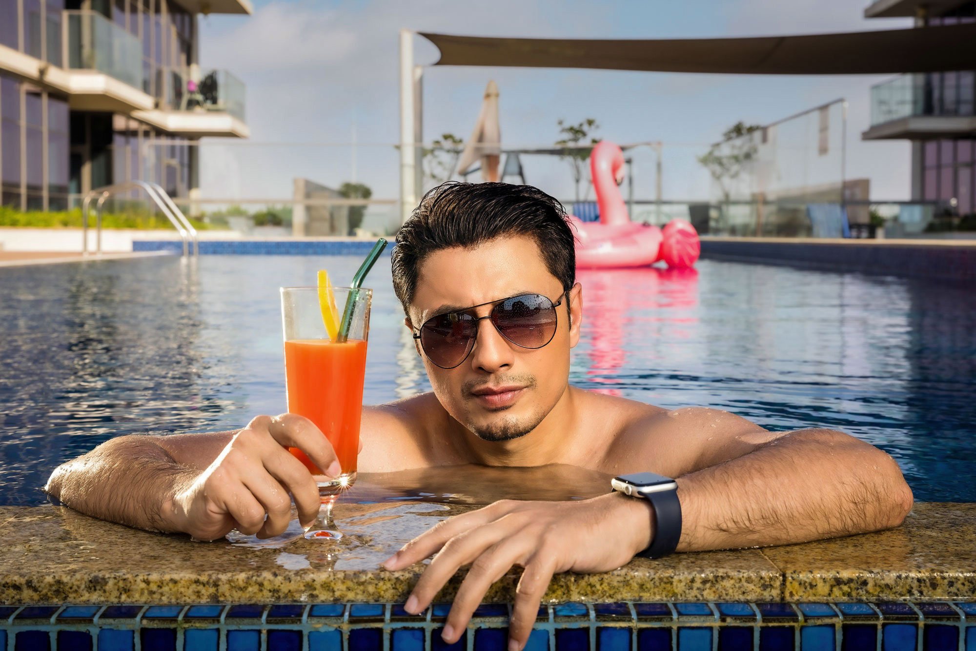 Lifestyle portrait of man relaxing by swimming pool with cocktail photographed for hospitality and lifestyle photography.