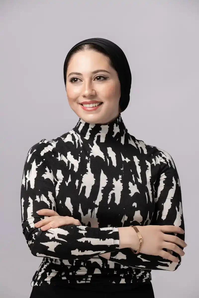 A man in a gray suit with glasses, sitting on a cream chair, holding a microphone, speaking during an event or panel.