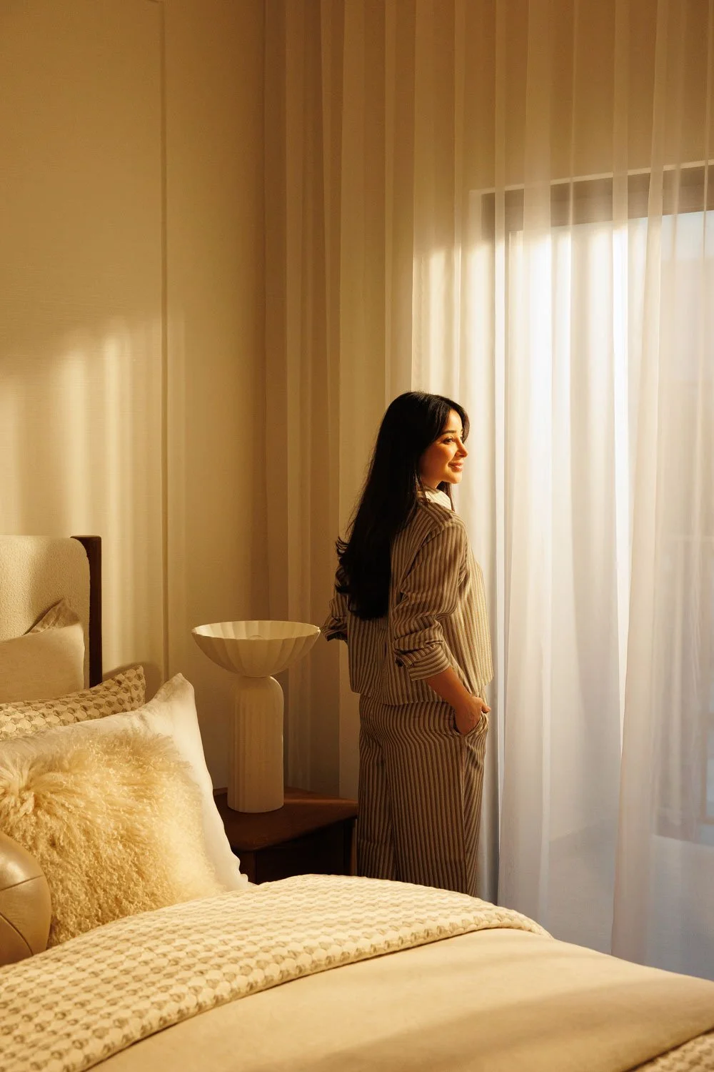 Natural lifestyle portrait of woman photographed in warm window light inside modern interior.