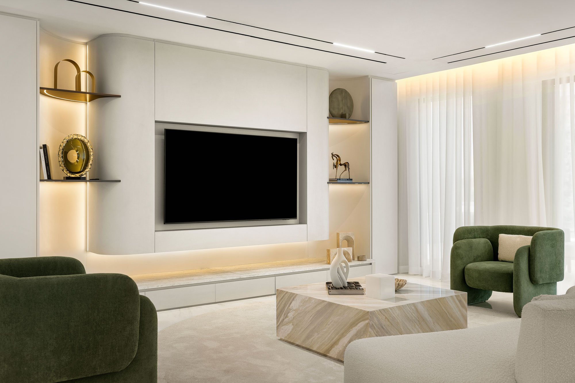 Modern living room with white walls, a large flat-screen TV, green armchairs, a marble coffee table, and built-in shelves with decorative items.