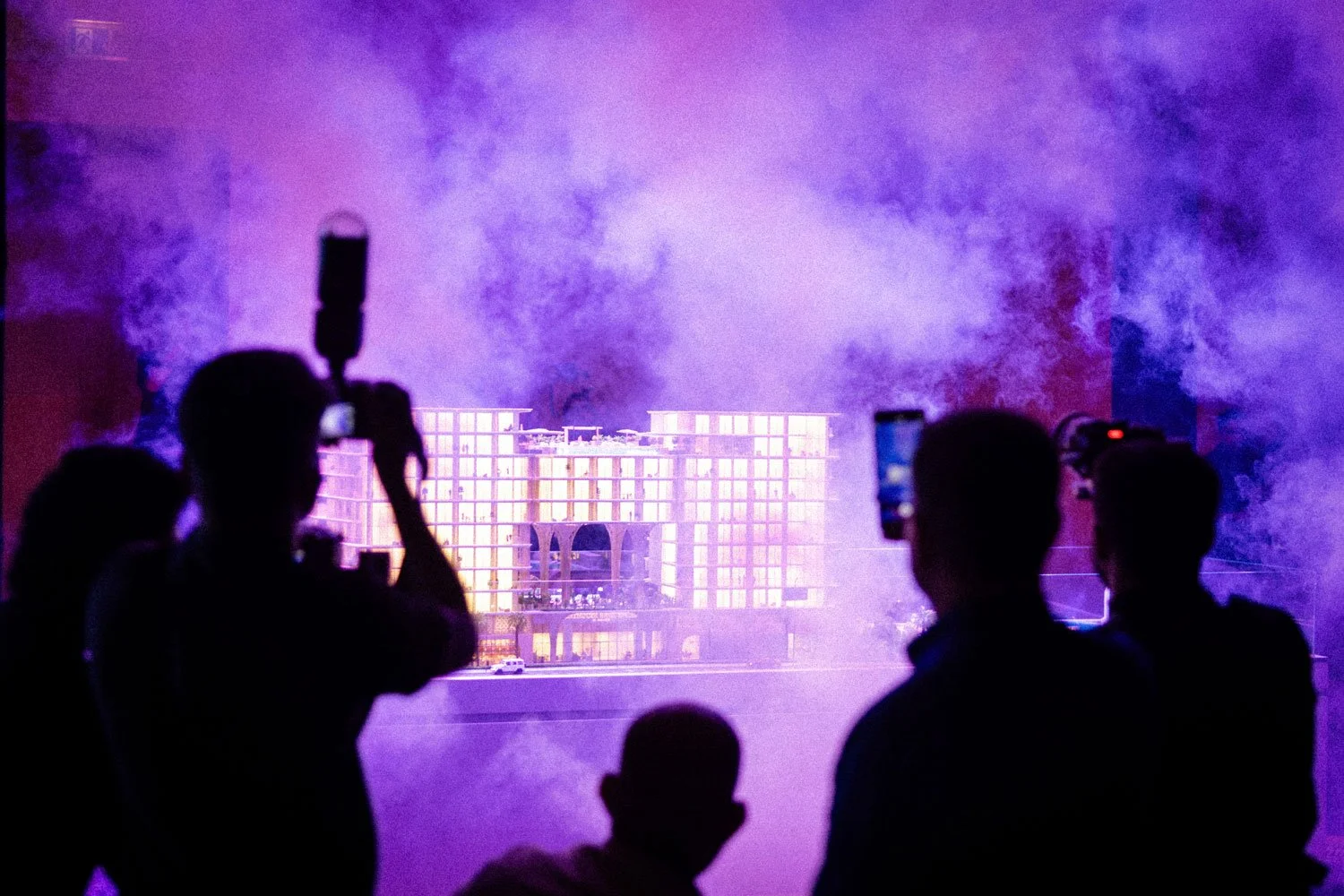 Silhouettes of people taking photos or videos of a building with colorful lighting and smoke effects.
