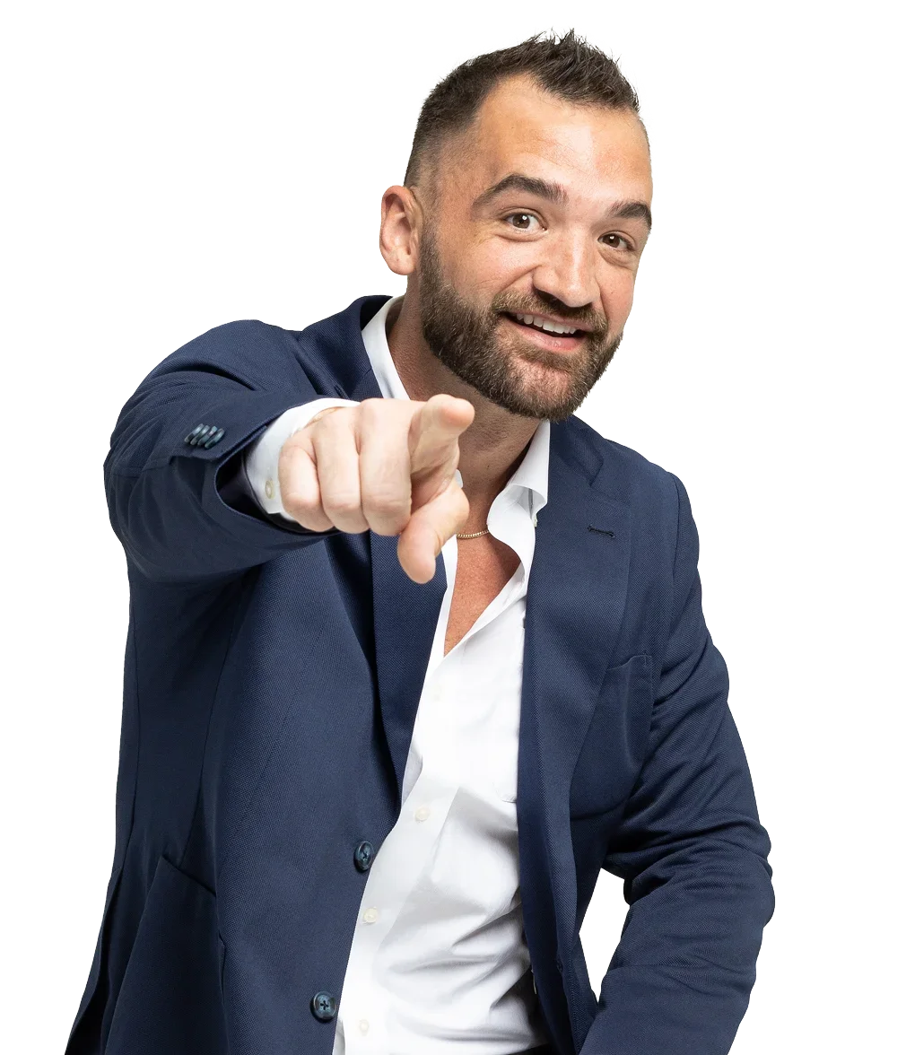 A man in a navy blue suit and white shirt smiling and pointing at the camera.