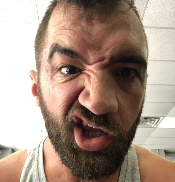A man with a beard making a funny, exaggerated facial expression in an indoor setting
