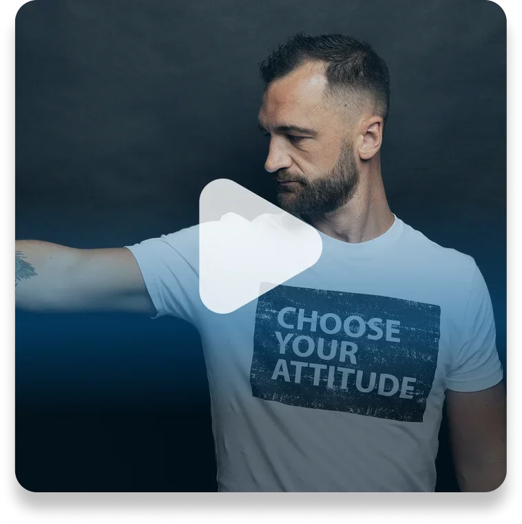 A man with a beard and short hair wearing a white T-shirt with the text "Choose Your Attitude" standing against a dark background.
