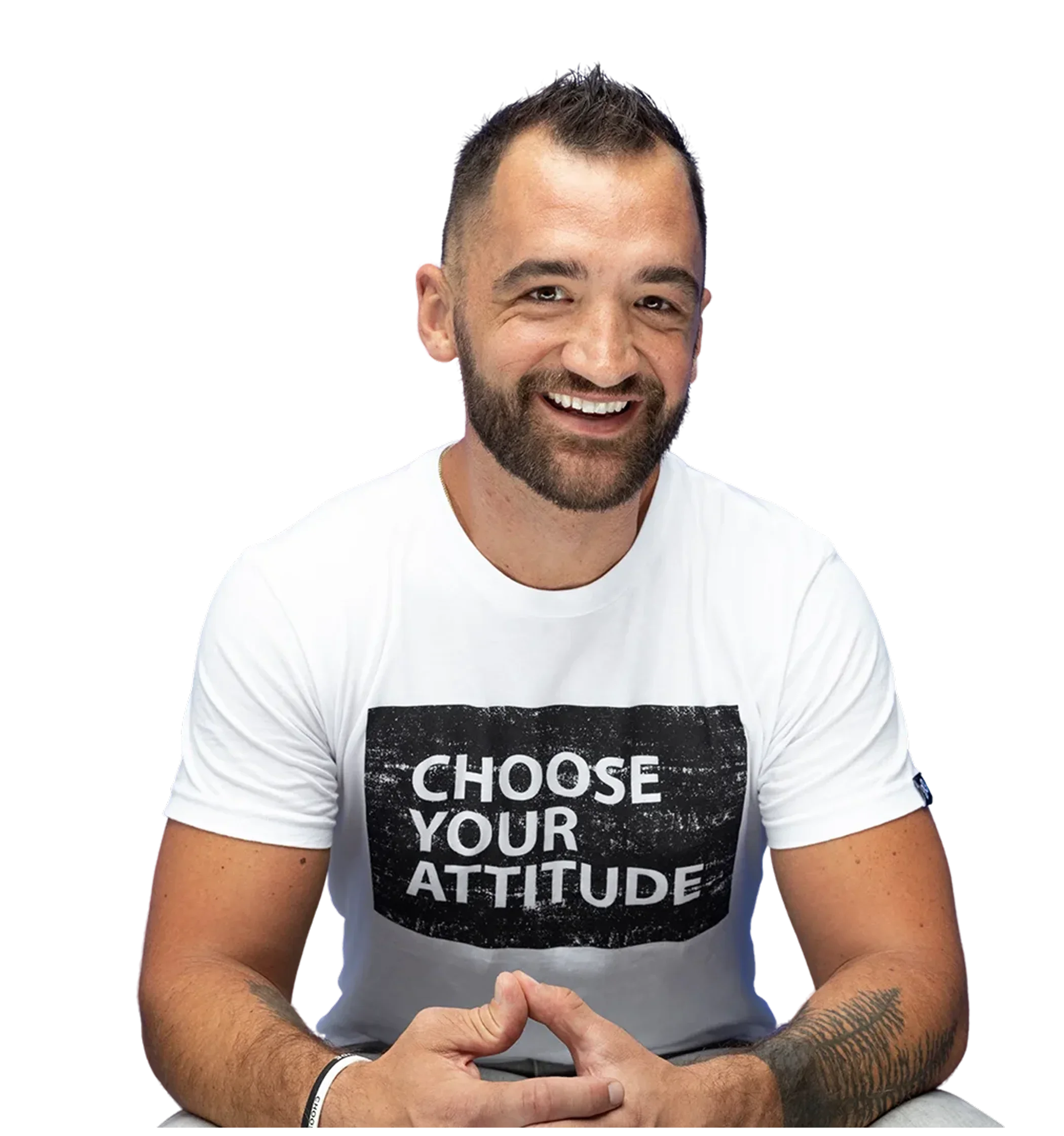 Smiling man with a beard wearing a white t-shirt that says "Choose Your Attitude" in black letters, sitting with hands clasped.
