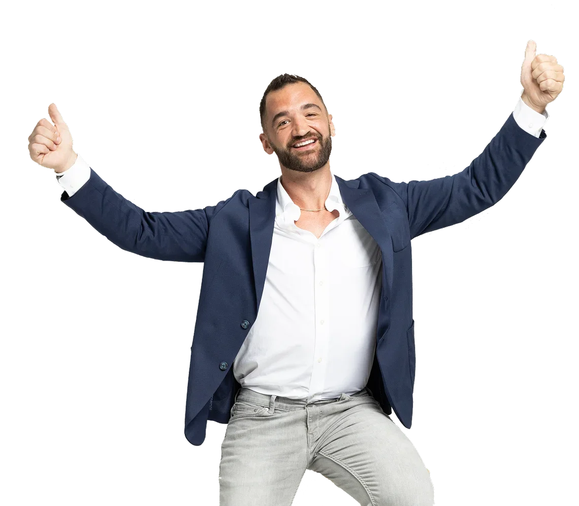 A man in a navy blazer and light-colored pants smiling with arms raised in celebration.
