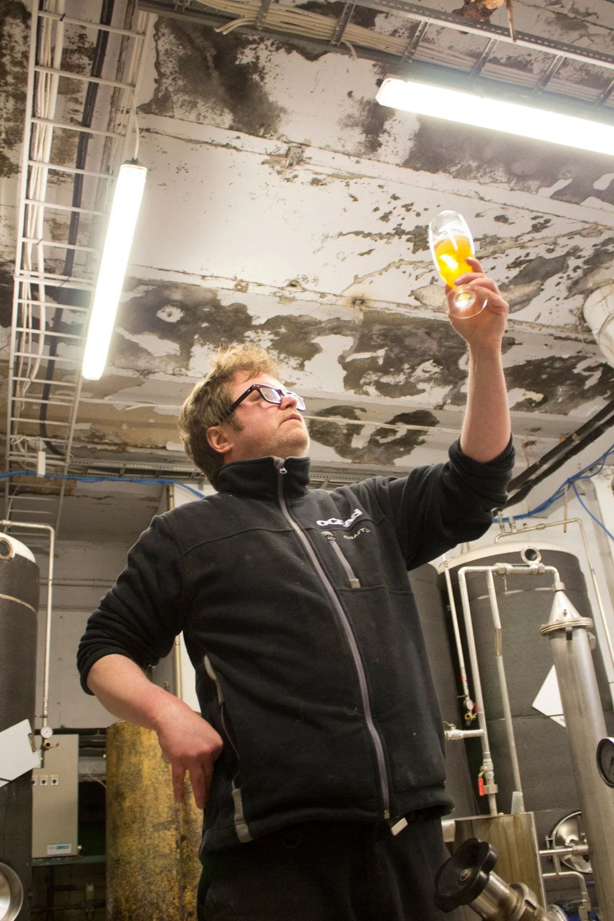 Man som håller ett glas öl högt i ett industriellt utrymme