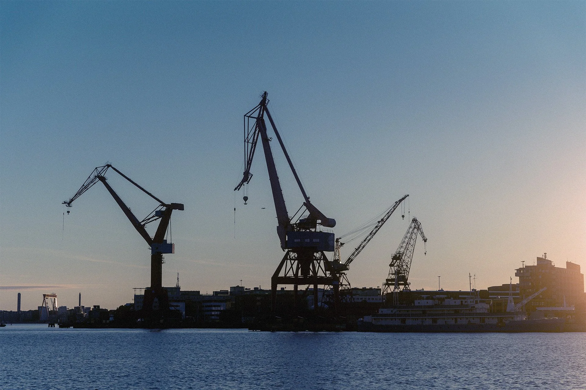 Silhuetter av stora industriella hamnkranar i göteborgs hamn och byggnader vid havet under solnedgången