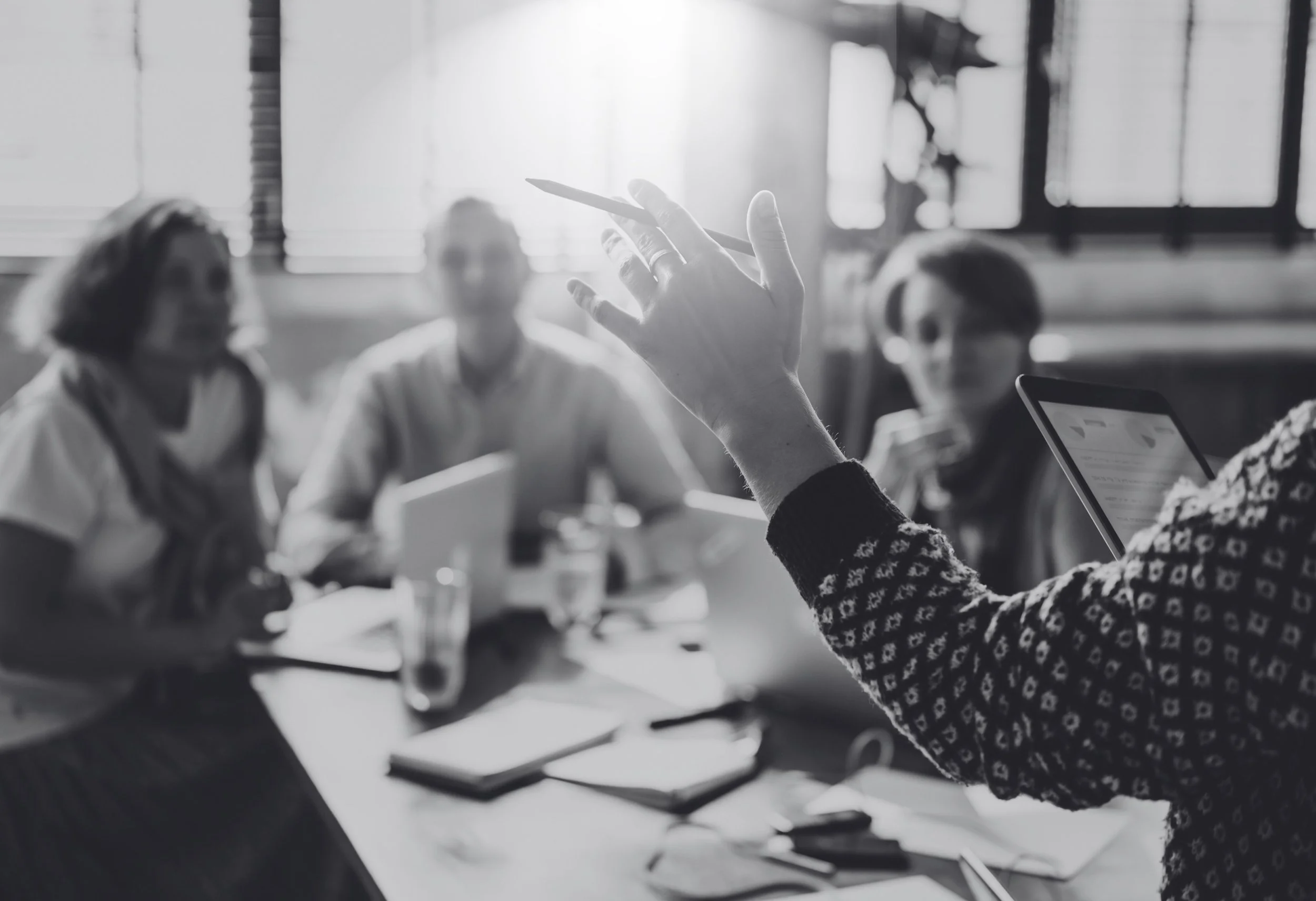 Groupe de personnes lors d'une réunion, une personne tenant un stylo en train de faire une présentation, scène en noir et blanc