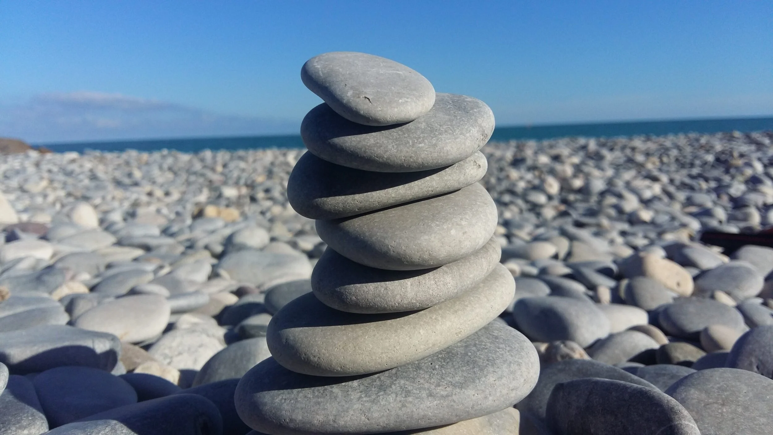Pile de neuf pierres plates sur une plage de galets avec la mer et un ciel bleu en arrière-plan.
