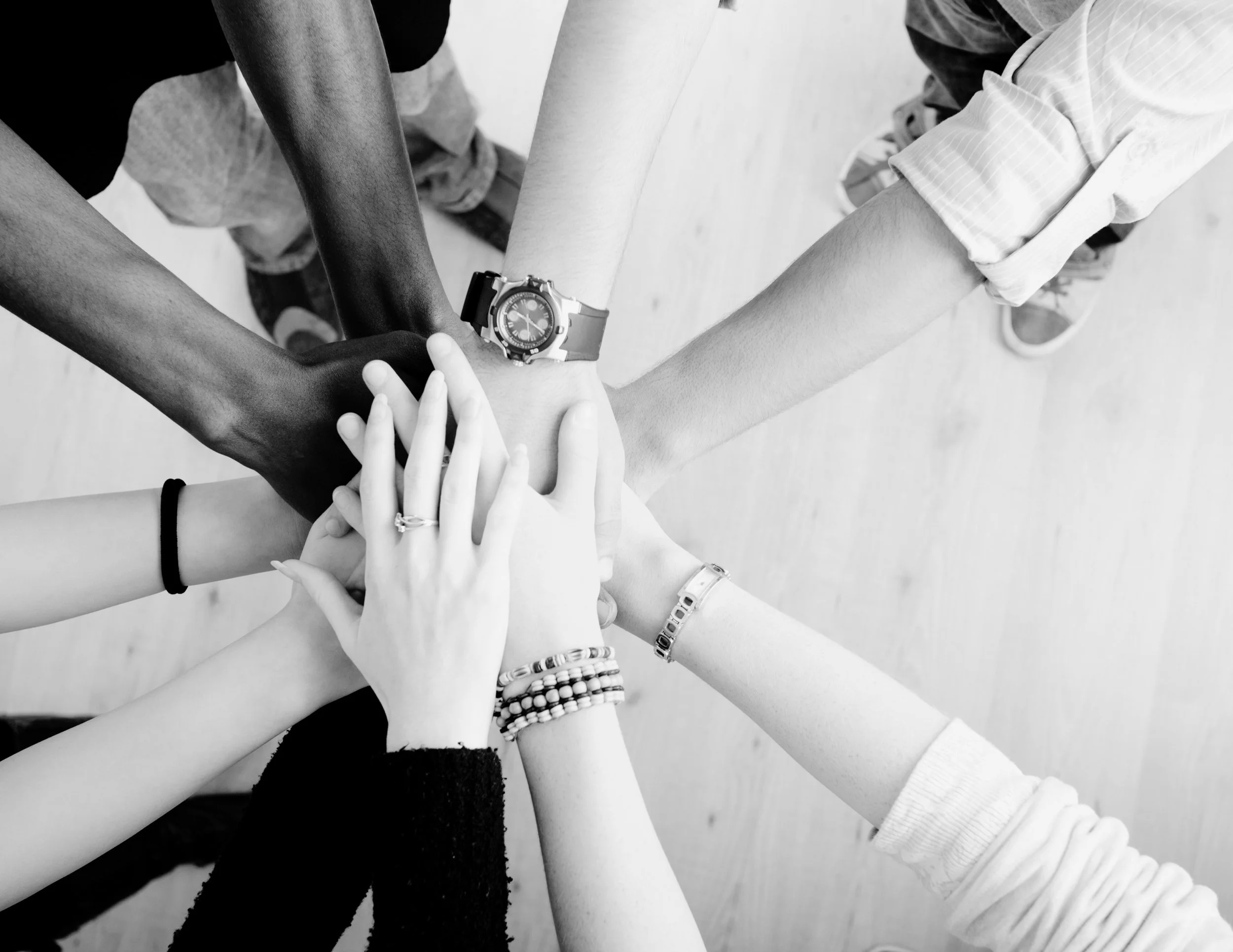 Plusieurs mains de différentes personnes se superposent pour former un cercle, symbolisant l'unité et la collaboration.