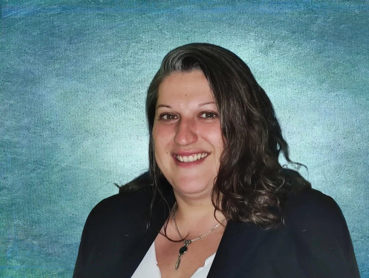 Une femme souriante avec des cheveux bouclés et portant une chaîne avec un pendentif, en fond bleu vert.