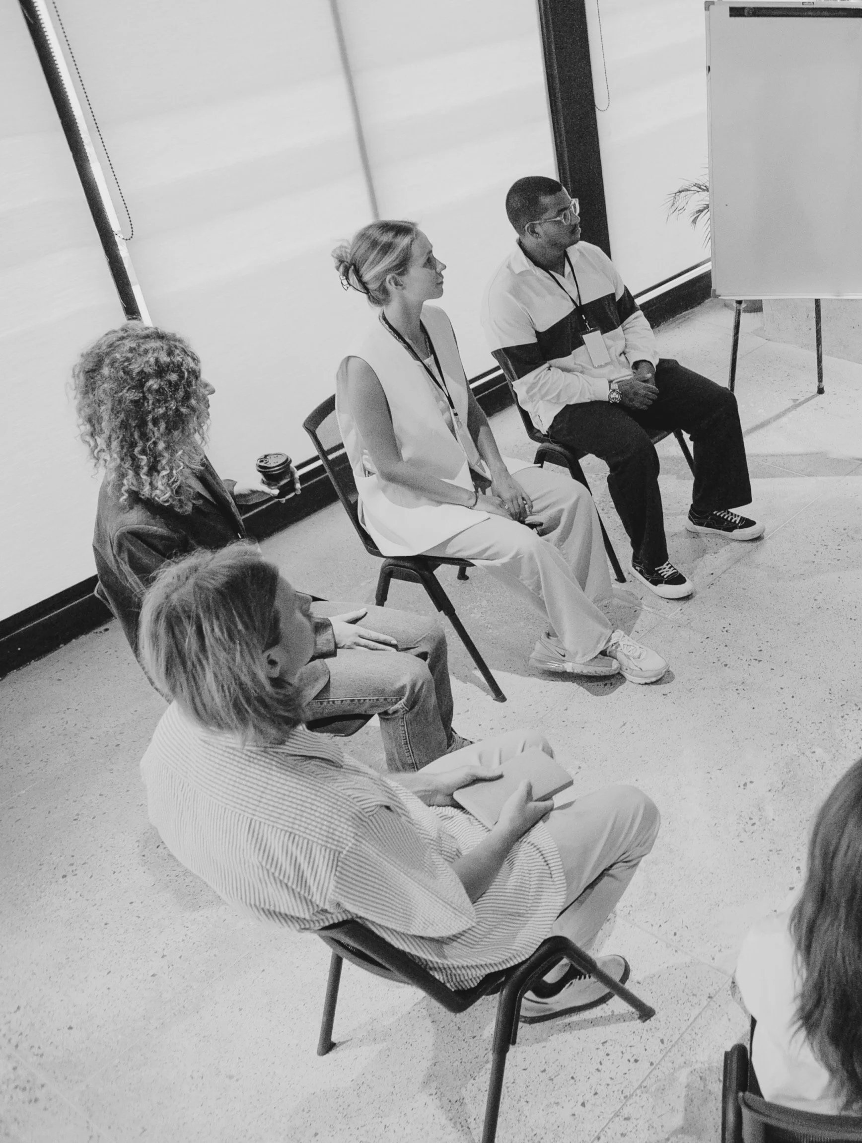 Groupe de cinq personnes participant à une séance de discussion ou de formation, assises sur des chaises dans une salle, avec un tableau blanc en arrière-plan.