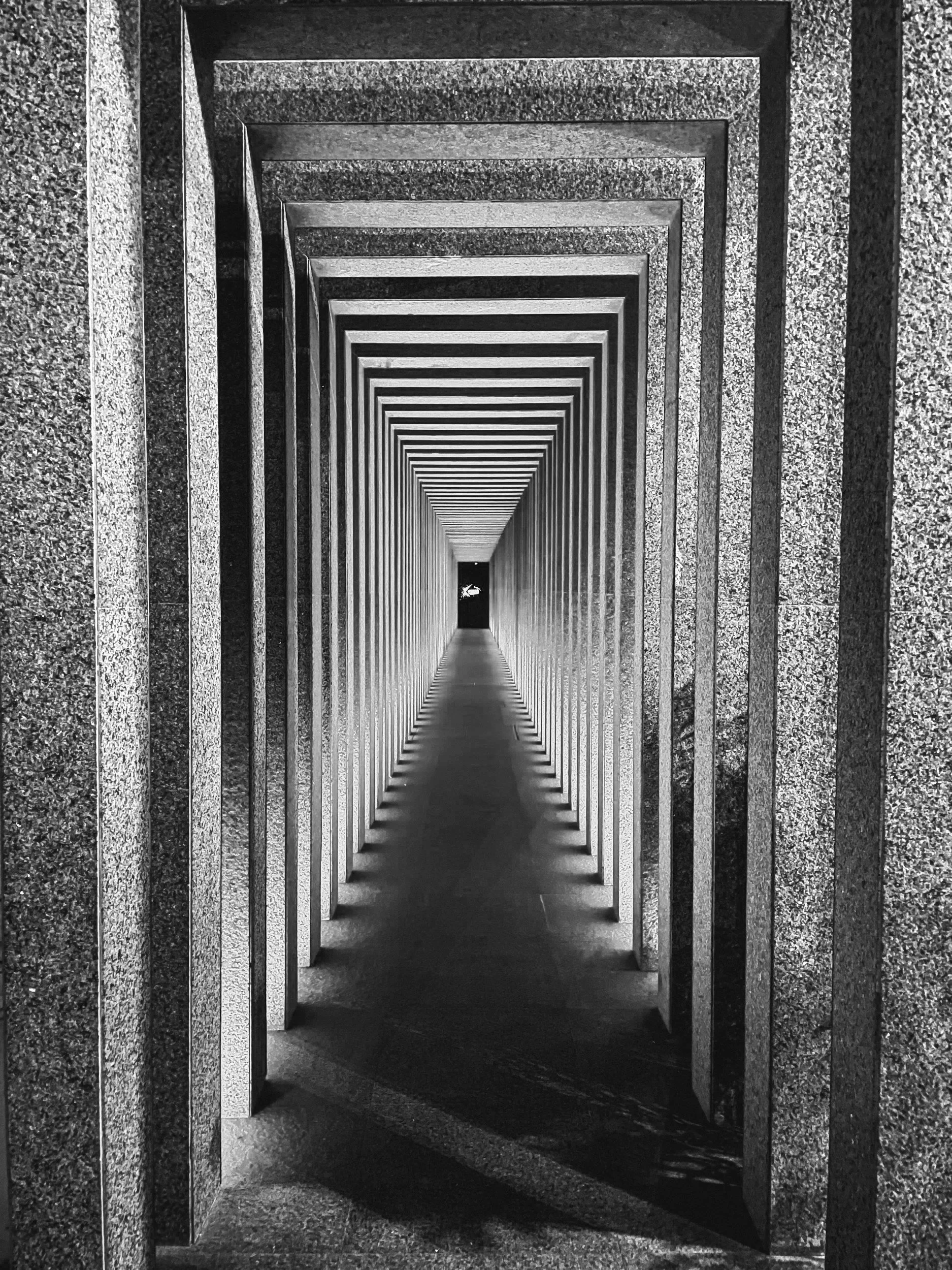 Passage étroit formé par une série de cadres rectangulaires en pierre, créant un effet de profondeur avec un point de fuite au centre, dans une structure en pierre.