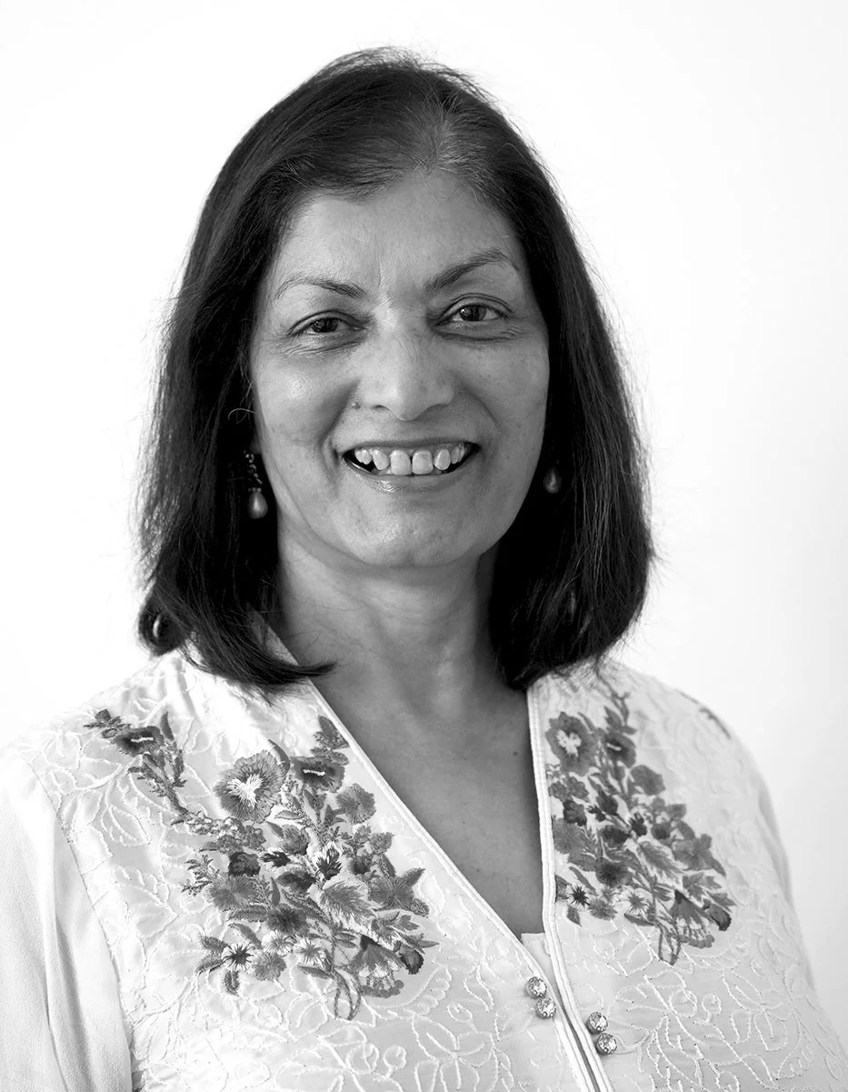 Black and white portrait of a woman with shoulder-length dark hair, smiling, wearing earrings and a embroidered top.