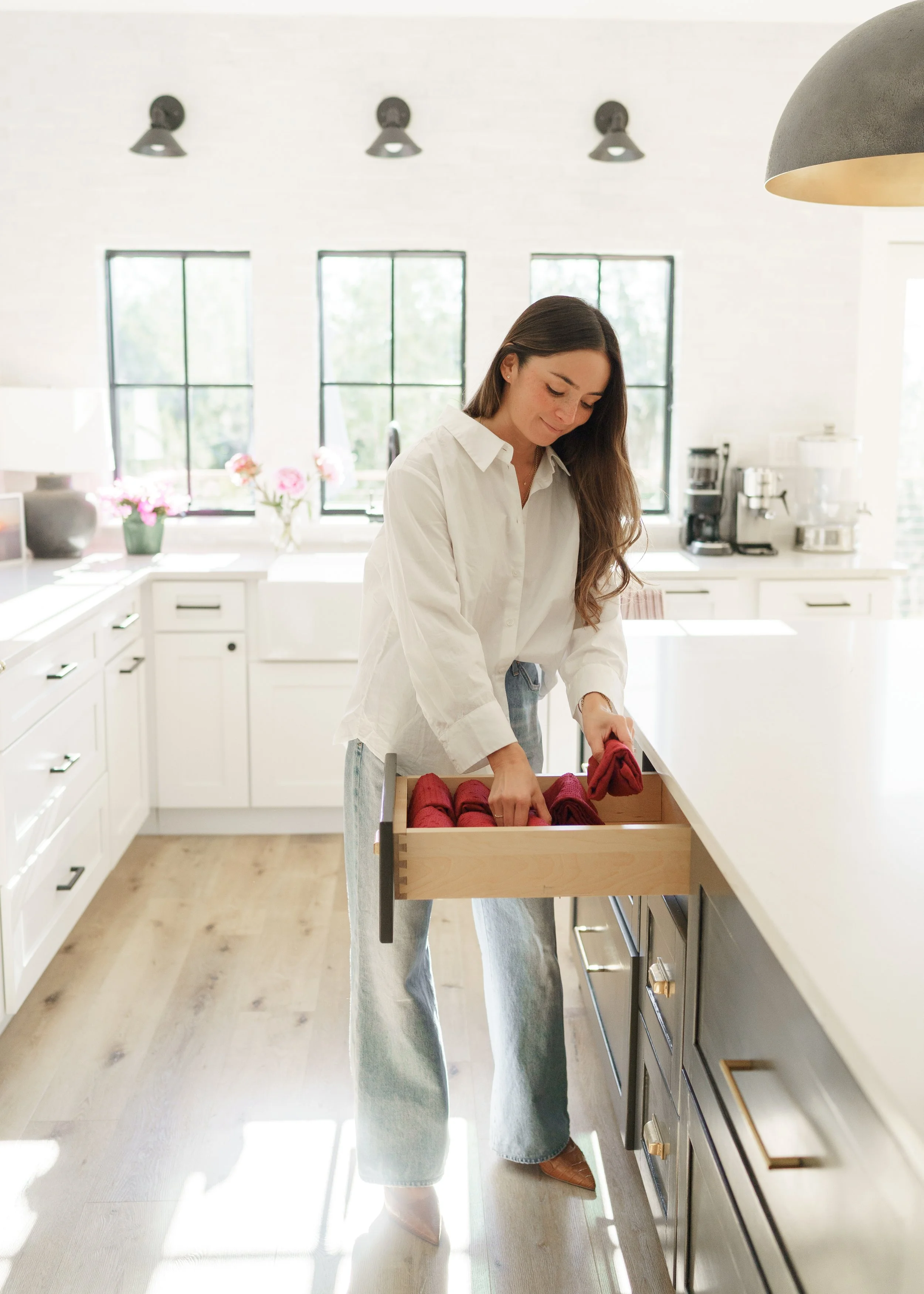 Woman opening a drawer with red cloth napkins in a bright modern kitchen.