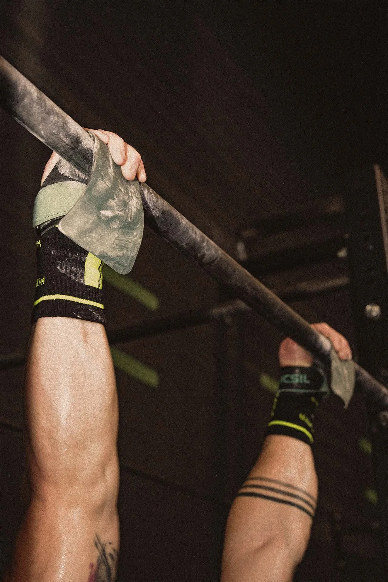 Persona haciendo dominadas en una barra, sosteniéndose con las manos y usando guantes de entrenamiento.