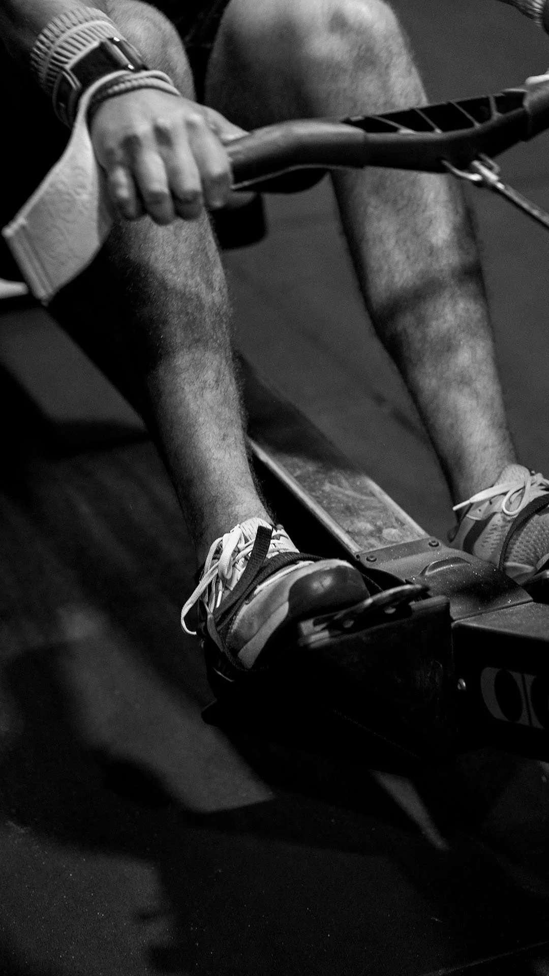 Persona en una máquina de remo, vista en primer plano, en un ambiente de gimnasio en blanco y negro.