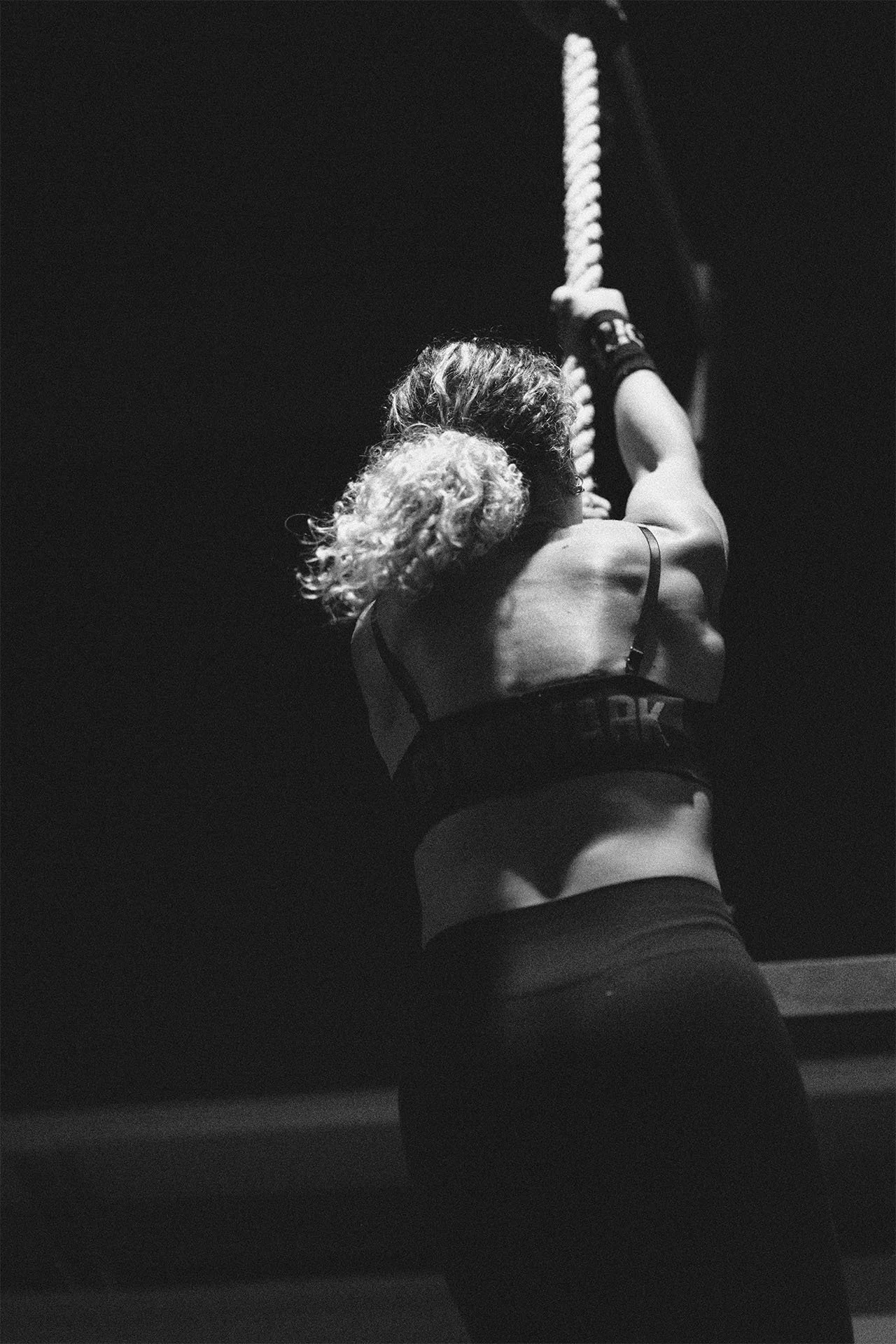 Mujer entrenando en un gimnasio, levantando una cuerda en un entorno oscuro en blanco y negro
