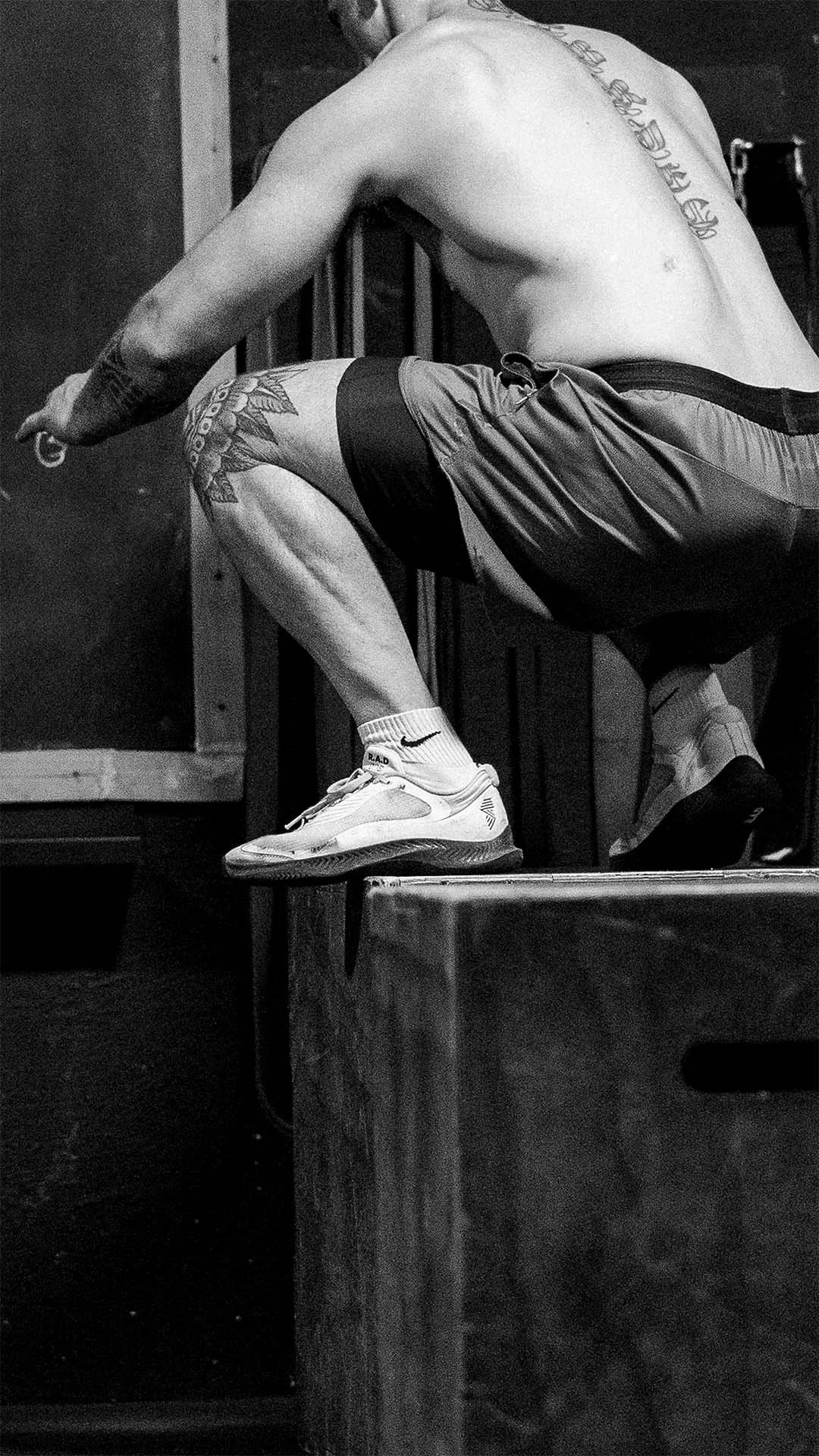 Hombre sin camiseta haciendo ejercicio en un gimnasio, en cuclillas, visto en negro y blanco.