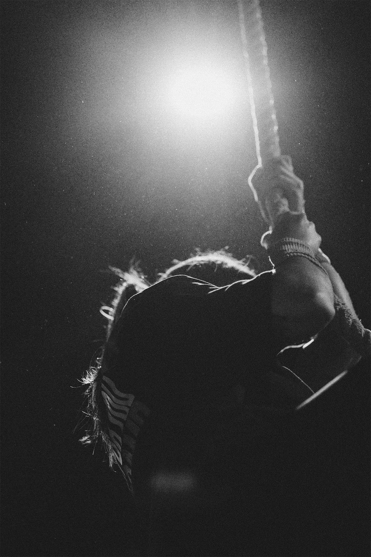 Persona sujetando una cuerda en el aire, vista desde abajo, en un entorno oscuro con una fuente de luz brillante detrás.