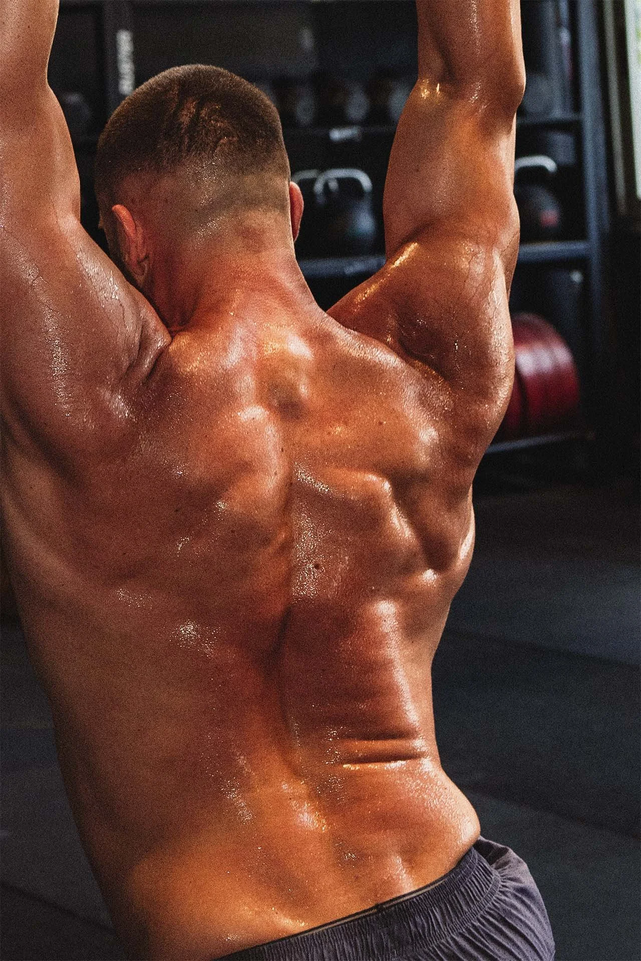 Hombre musculoso con piel sudorosa levantando pesas en un gimnasio.