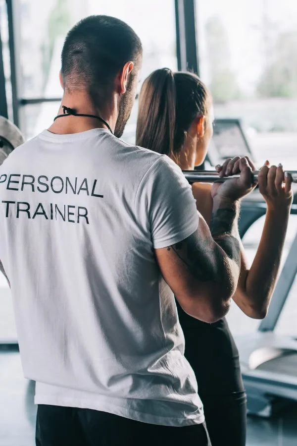Un entraîneur personnel aide une femme à faire un exercice de musculation avec une barre à la salle de sport.