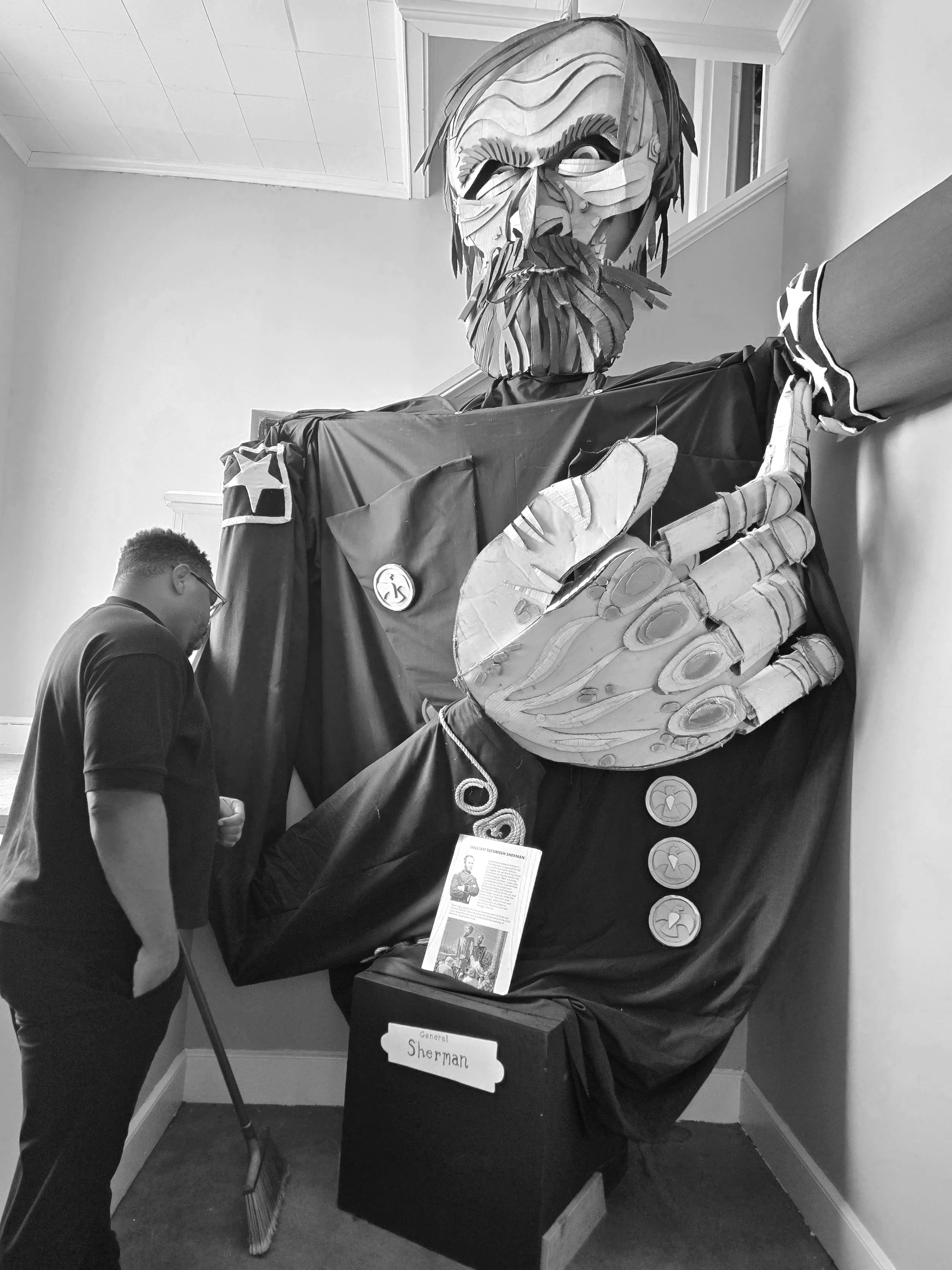 A large paper mache sculpture of William Tecumseh Sherman, a Civil War general, on display at an indoor event. The sculpture features his face with detailed hair and beard, and a costume with buttons and stars. A person is standing nearby, observing the sculpture.