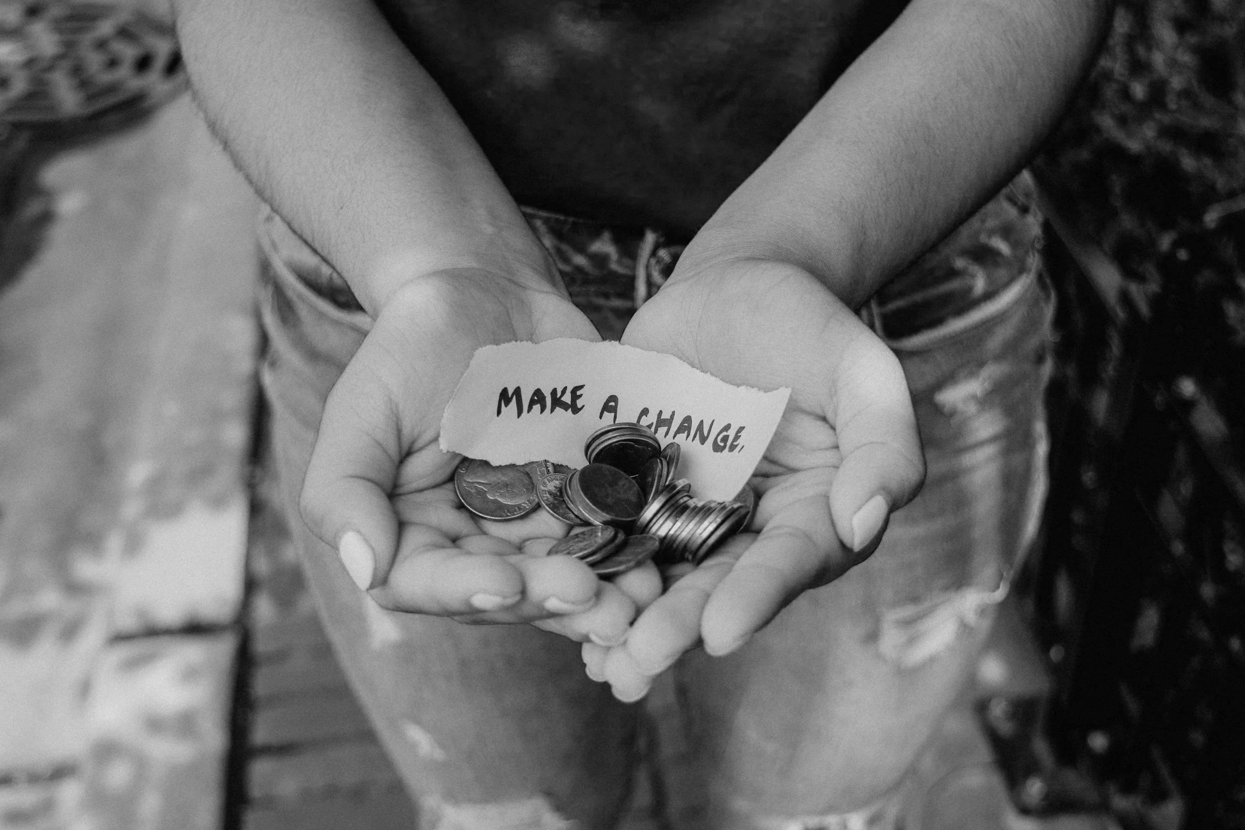 A person holding a handful of coins and a torn piece of paper with the words 'Make a Change' written on it.