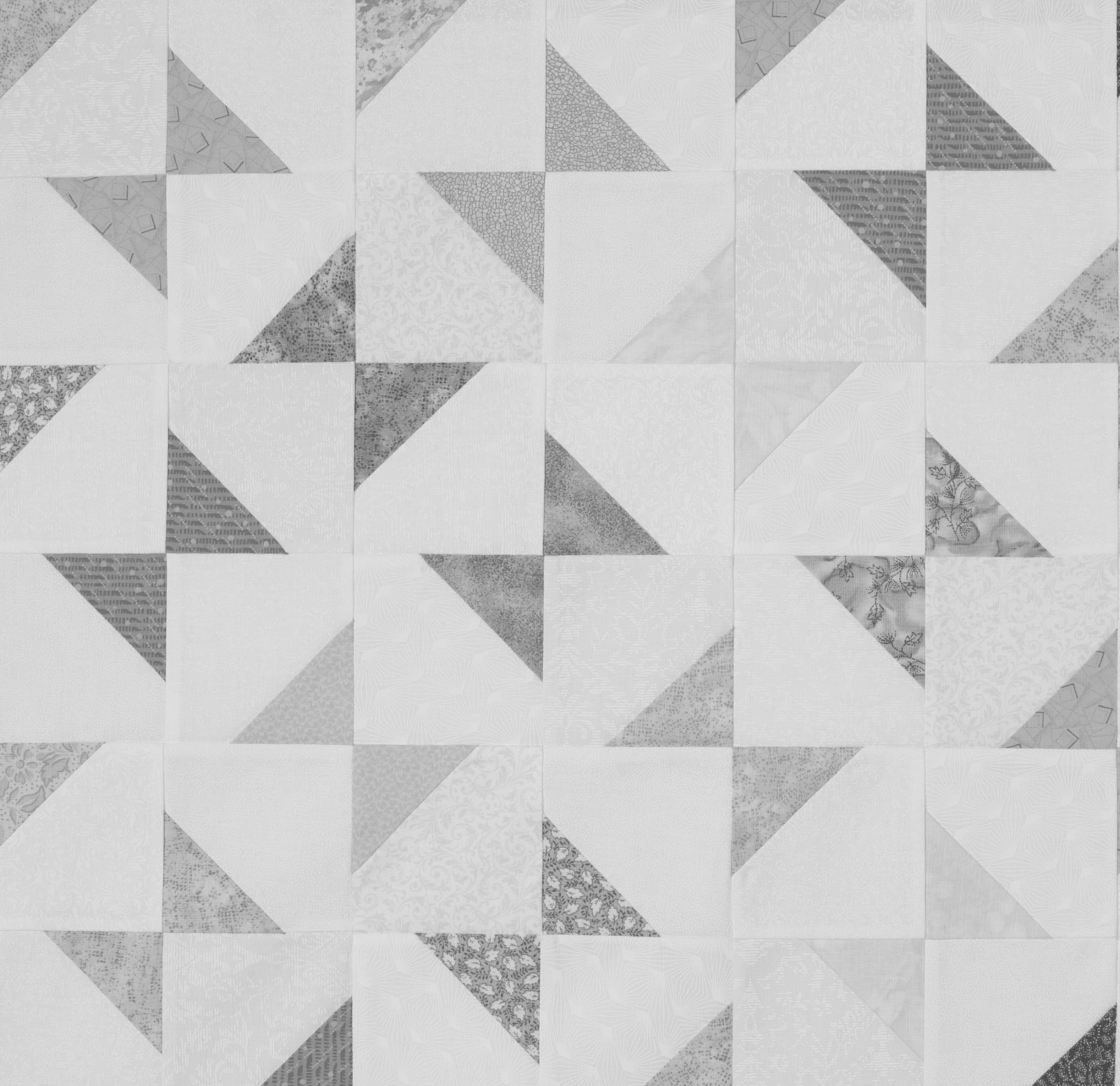A quilt with a geometric pattern of triangles and squares in shades of gray and white with various textured and patterned fabrics.