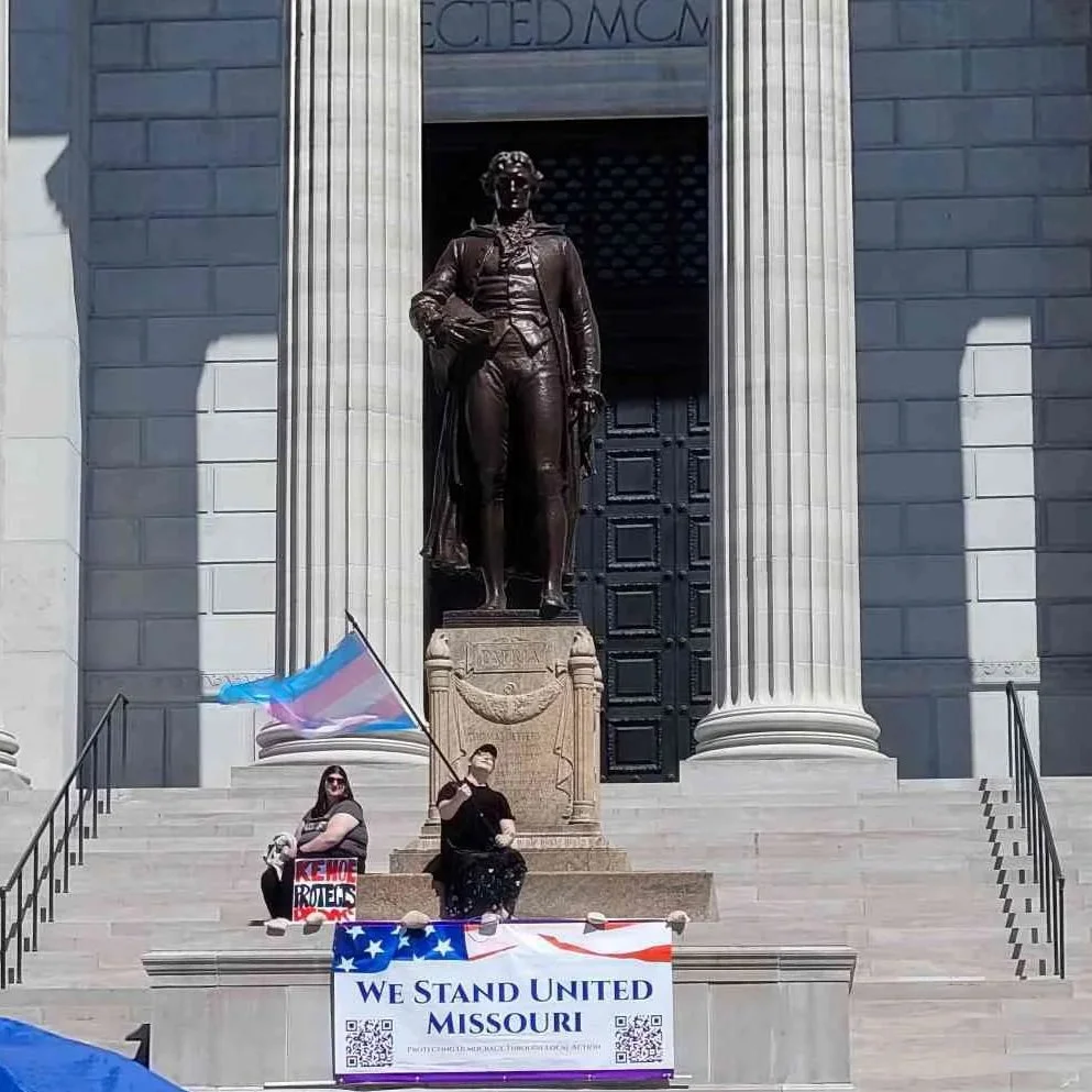 IN•TACT Chair Advocate waves Trans Flag on the steps of the Missouri Capitol in front of statue of Thomas Jefferson at No Kings III on 3/28/2026