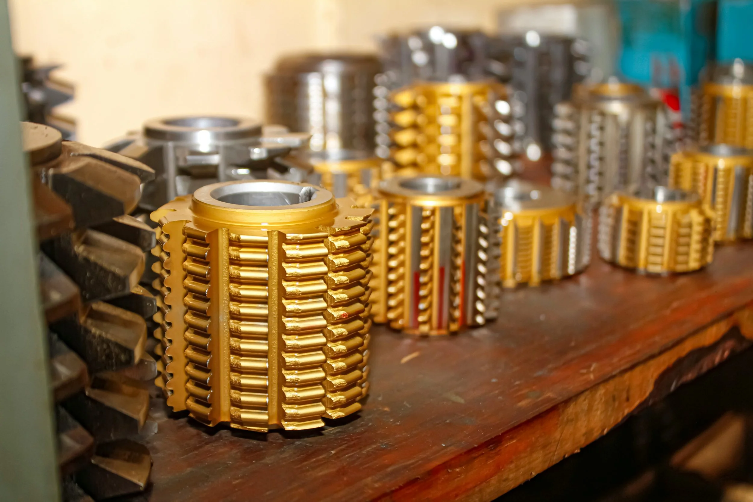 Various metallic machining parts with gold and silver finishes arranged on a wooden workbench.