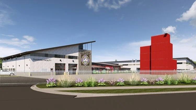A modern police training facility with a gray and red exterior, featuring a large police badge sign, open garage bays, and landscaped purple flowers in front.