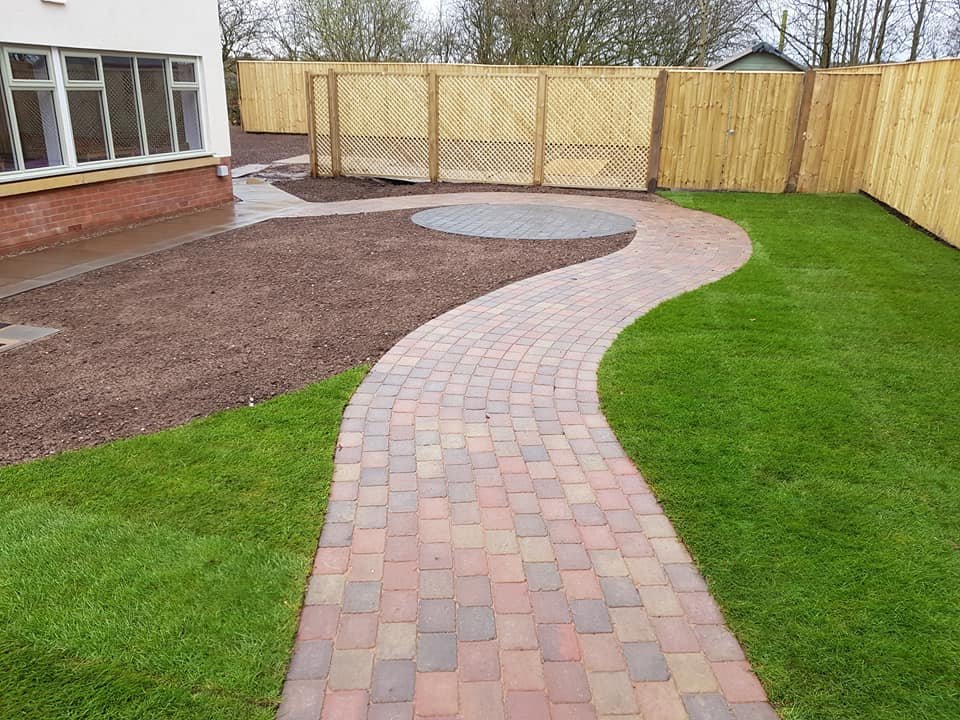 Curved brick pathway leading to a backyard with a grassy area and a fenced yard.