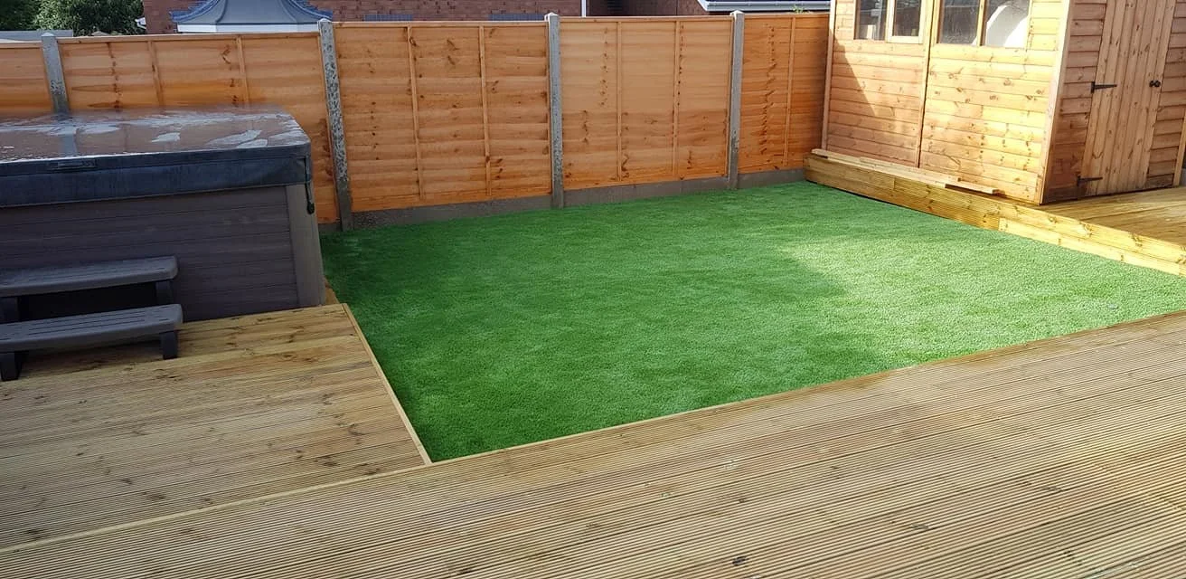 Backyard with a wooden deck, a green artificial grass area, a hot tub, and a wooden fence and shed.