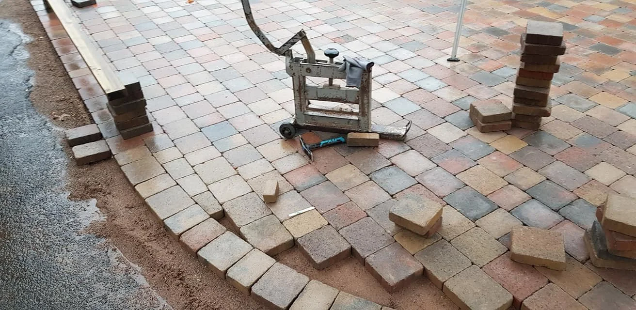 Vast area of brick pavement under construction with scattered bricks, stacking piles, and a tile cutter in the middle.