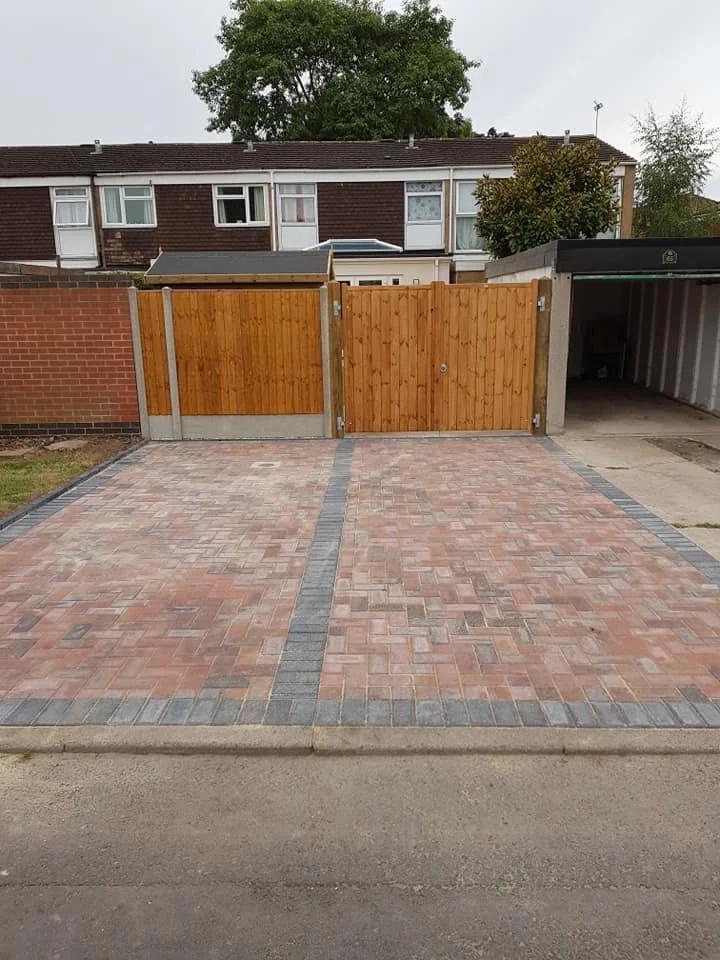 Empty driveway with brick pattern, wooden fence, and garage in the background