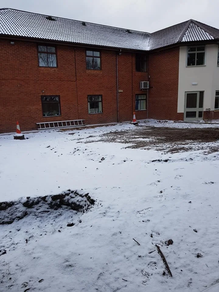 An apartment building with a snowy yard in front, construction cones, and a ladder leaning against the brick wall.
