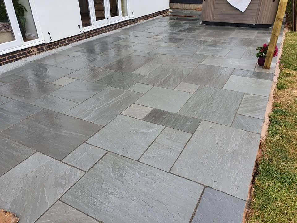 Refinished gray stone patio outside a house with a flower pot and a wooden post