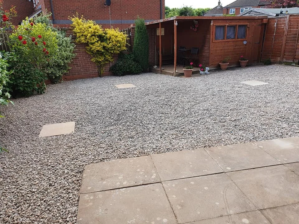Backyard with gravel ground, potted plants, and a wooden shed with outdoor furniture.