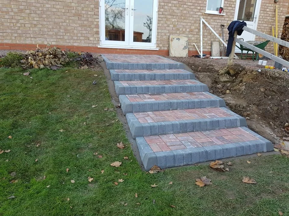 Newly constructed brick and stone steps leading up to a sliding glass door at a residential house, with construction materials and dirt around.