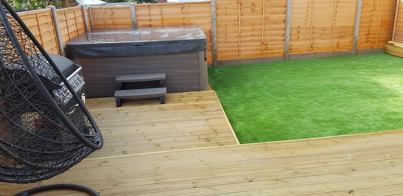 Backyard with a hot tub, small wooden steps, a grill, a hanging egg chair, a grassy area, and a wooden fence.