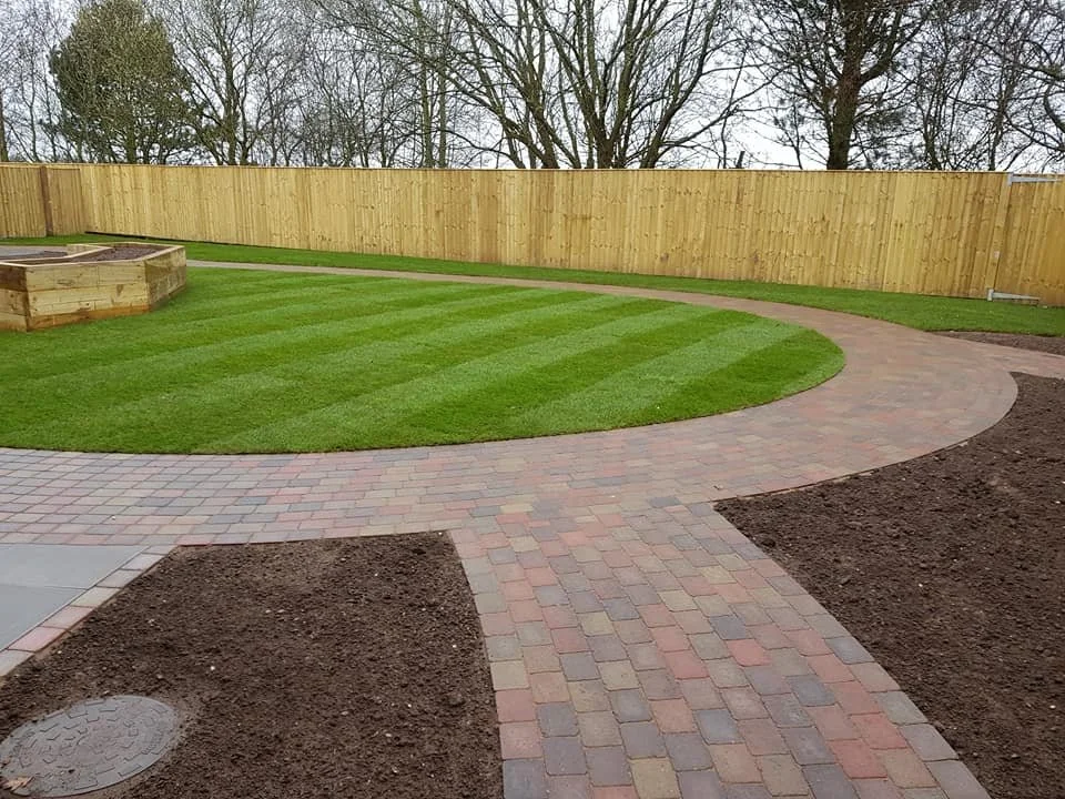 Newly laid brick driveway and pathway in a backyard with a wooden fence and green grass.