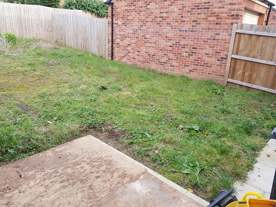 Small backyard with a patch of grass, a concrete patio, a wooden fence, and a brick house wall.