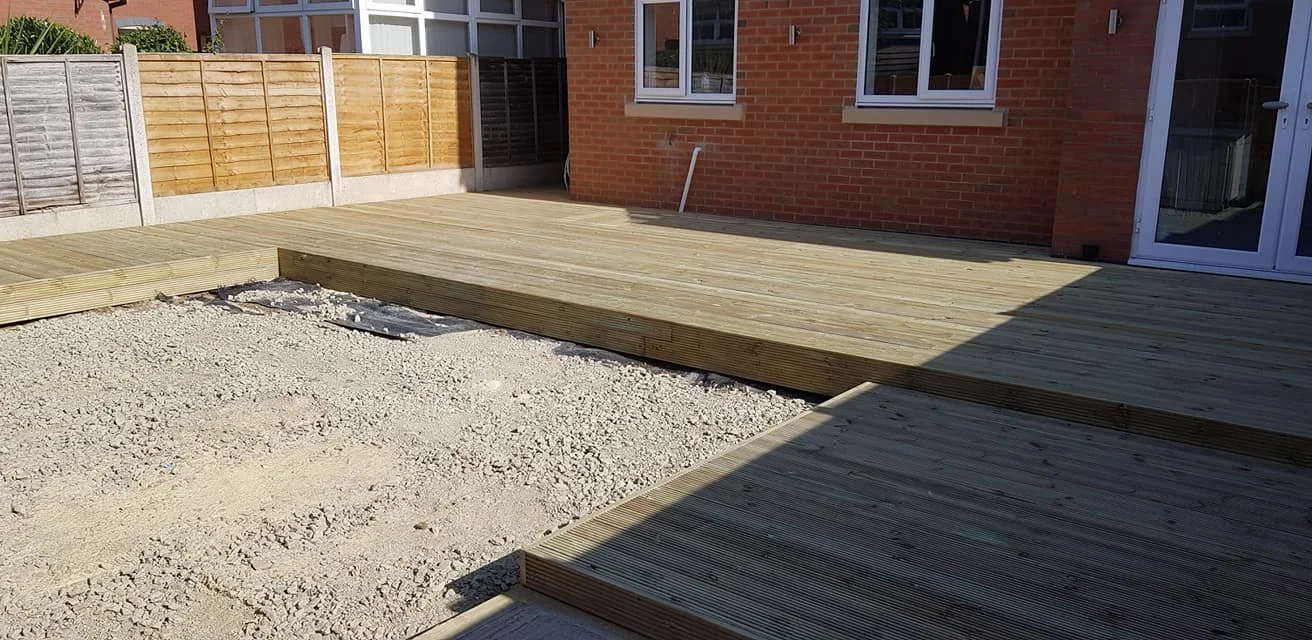 Newly constructed wooden deck with stairs in a backyard, surrounded by a fence, with a brick house in the background.