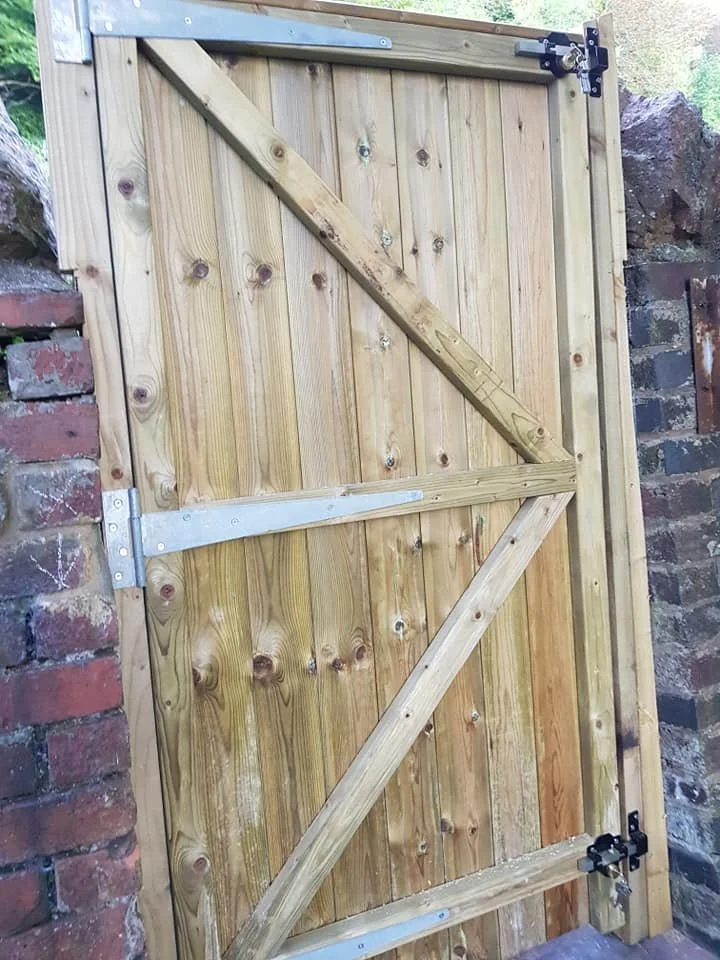 A wooden barn door with metal hinges and braces, installed between brick and stone walls.