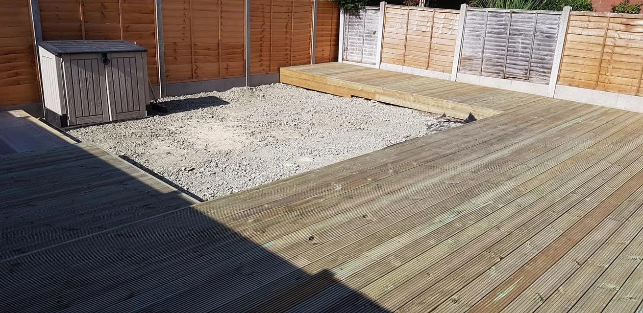Backyard with wooden deck and gravel area, fenced with wooden panels, and a storage shed in the corner.