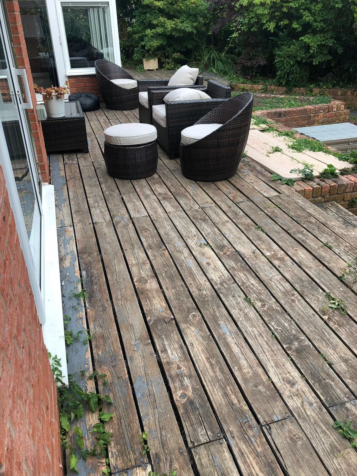 Outdoor patio with wooden decking, black wicker furniture with white cushions, and surrounding greenery.